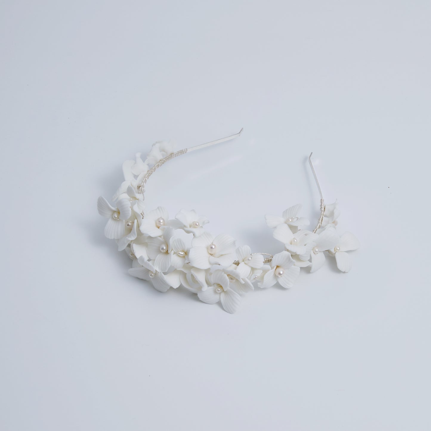 A gloriously romantic hand-sculpted porcelain bridal crown. Made with an arrangement of individually crafted flowers and dainty pearls. This full and textured headband makes a statement but yet still feels incredibly feminine.