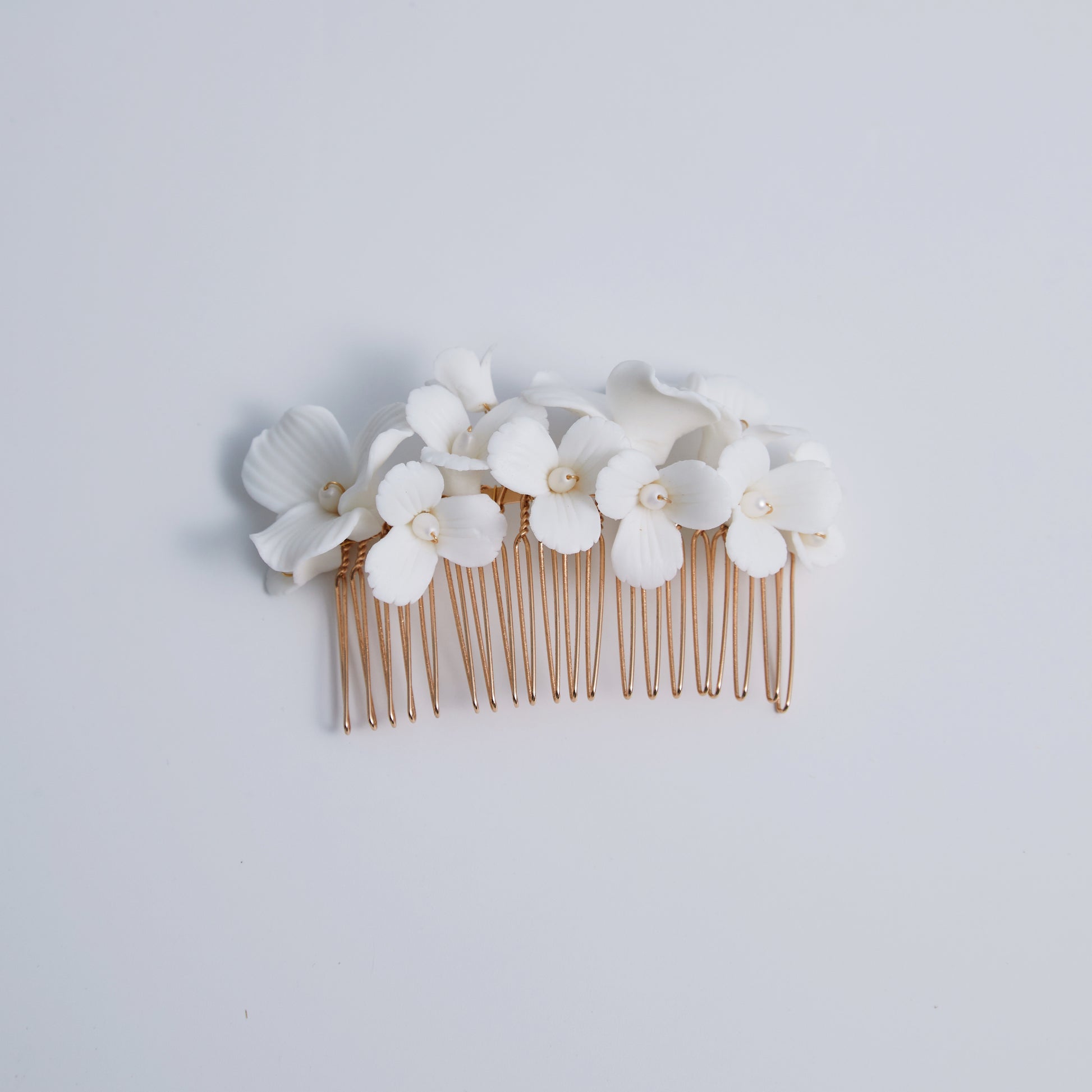 A delicate and romantic white porcelain bridal hair comb, handcrafted with love. This exquisite bridal hairpiece features a cluster of beautiful flowers adorned with lustrous natural freshwater pearls, arranged in a full design.