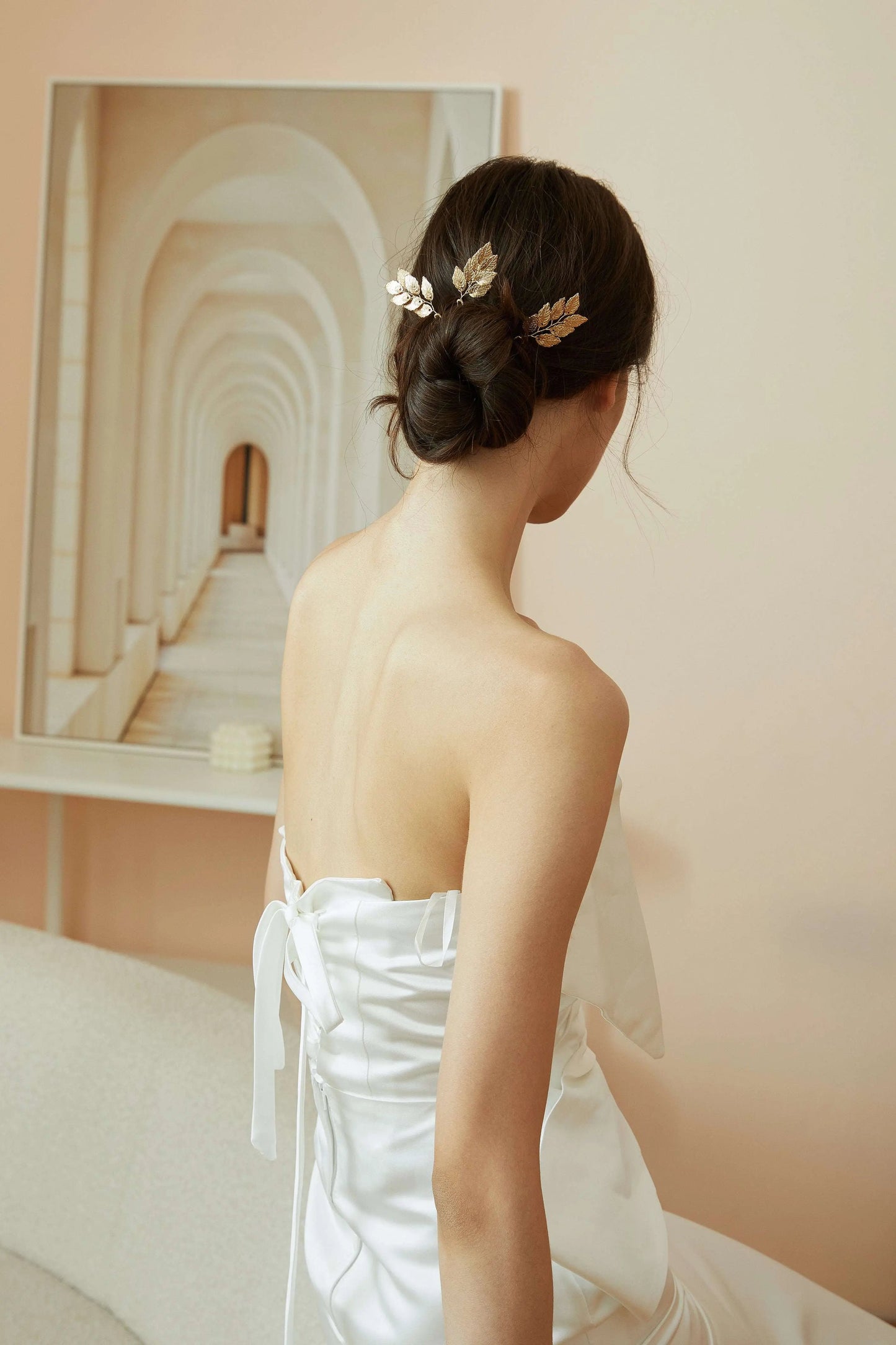 Bride in a white dress showing how to style minimalist gold and silver leaf hair pins in an updo