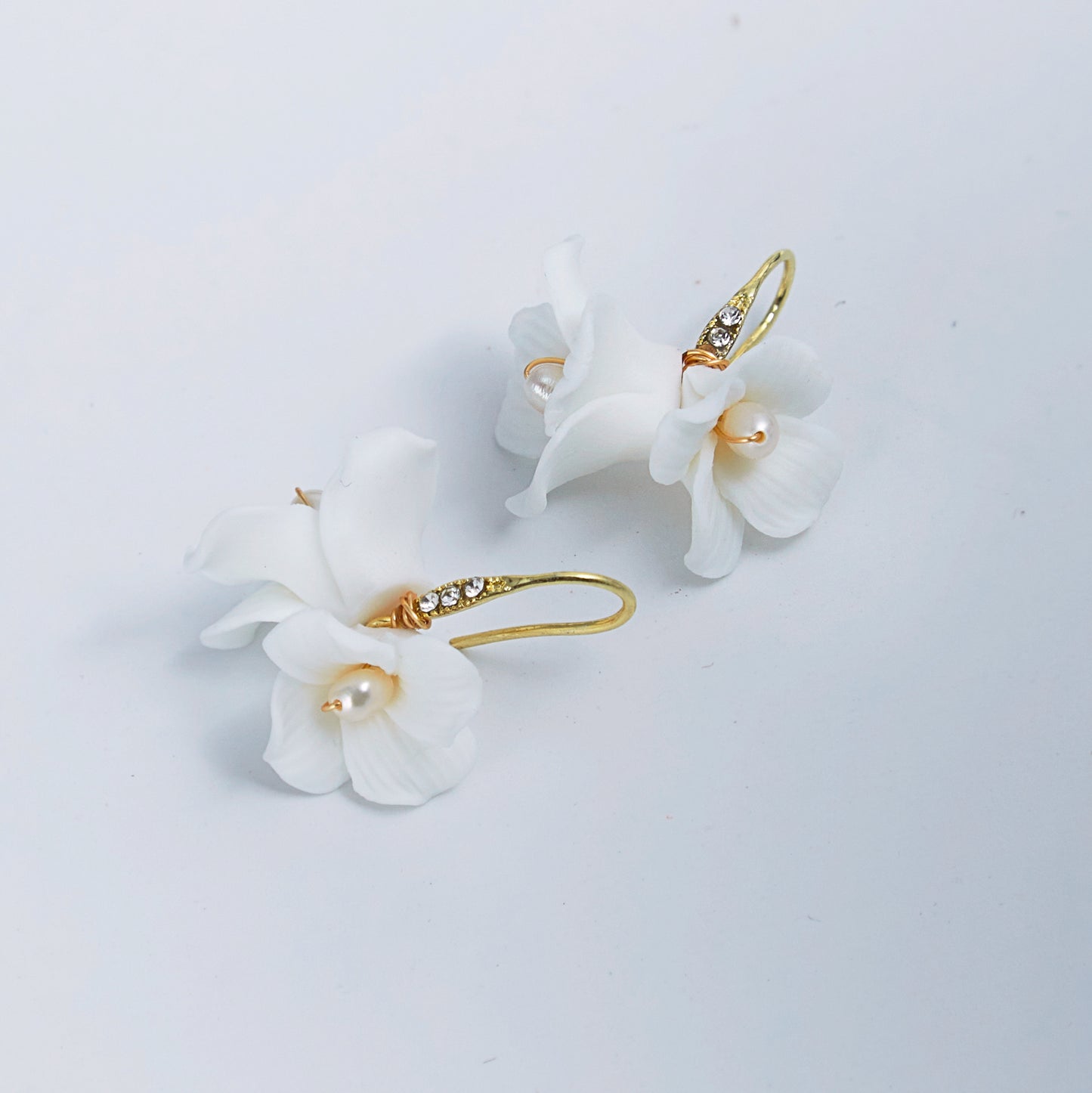 these flower bridal earrings feature two delicate white clay flowers adorned with freshwater pearls and crystal-embellished French hooks that create a brilliant sparkle with every move.