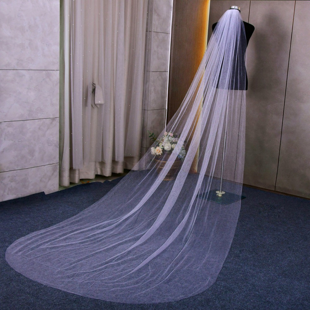 Luxurious single-layer cathedral wedding veil crafted from delicate sparkle glitter tulle. With an ivory base (also available in white and champagne), it features a simple cut edge for an elegant and timeless style that complements any bridal look.  At 3 meters long, this veil is the perfect bridal accessory to enhance any wedding dress. Offering a subtle sparkle without any fuss, it adds a touch of glamour to your special day.