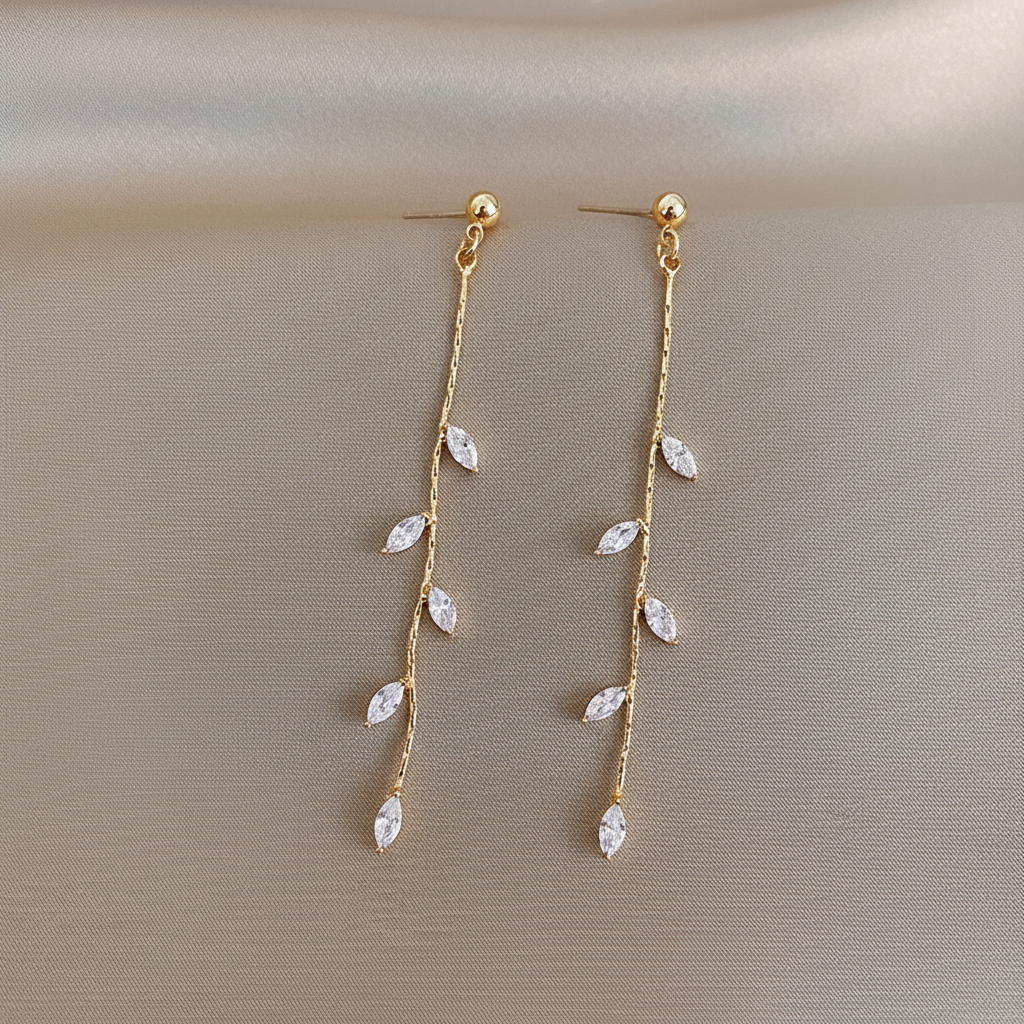 14K gold olive leaf crystal drop earrings flat lay top-down view on champagne silk