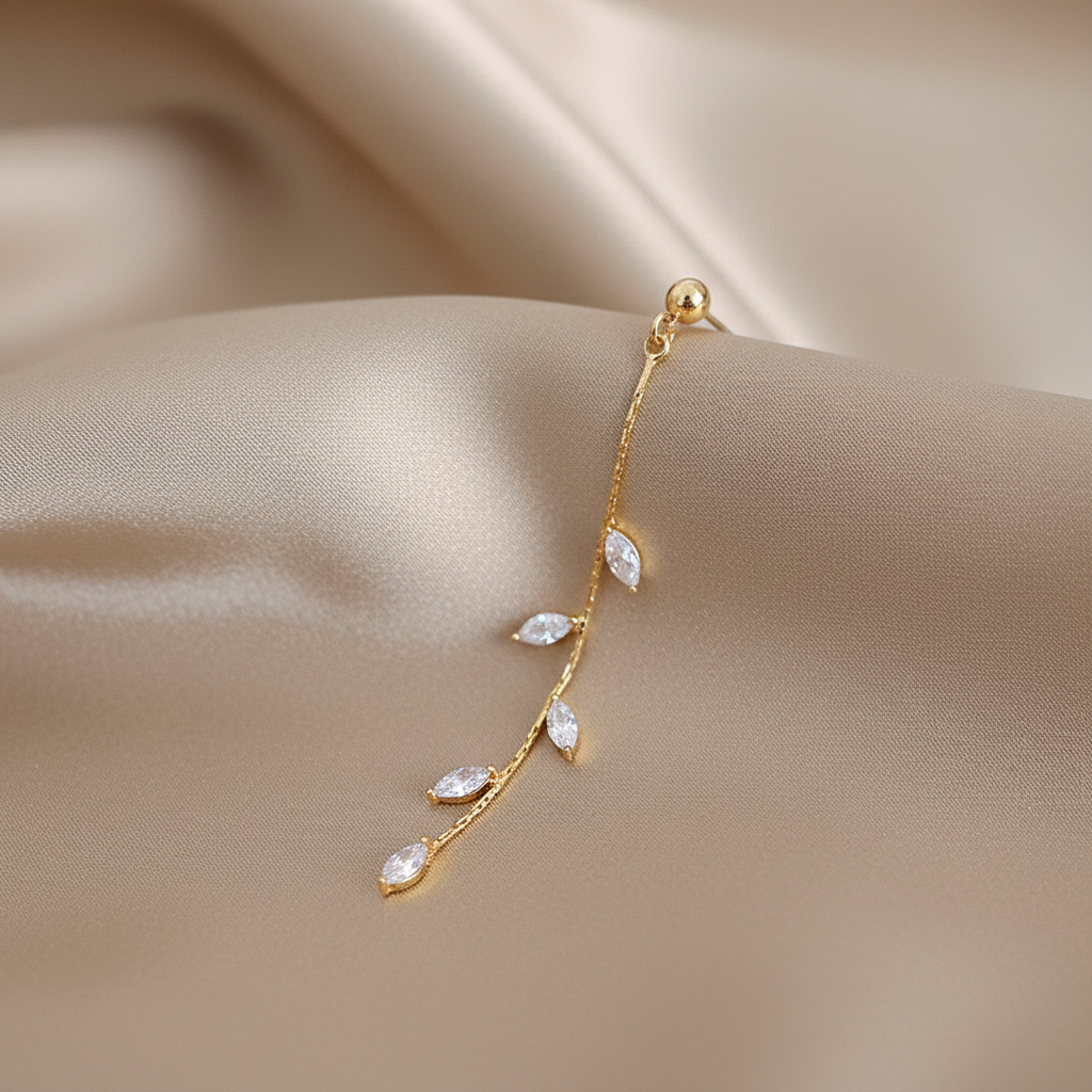 Single 14K gold olive leaf crystal earring detail shot on champagne silk