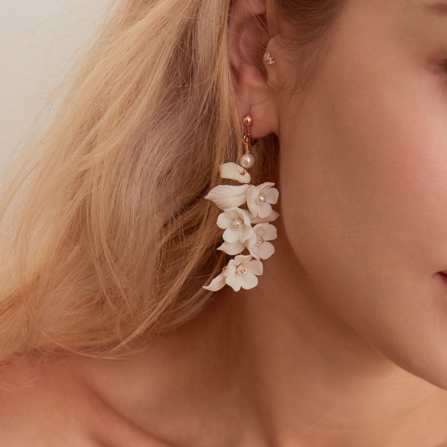 Carefully crafted by hand, these flower bridal earrings are a perfect match to our porcelain headpieces. Each earring features delicate white clay flowers and leaves adorned with shimmering freshwater pearls. These earrings have a long drop design that is sure to catch attention and make a statement.