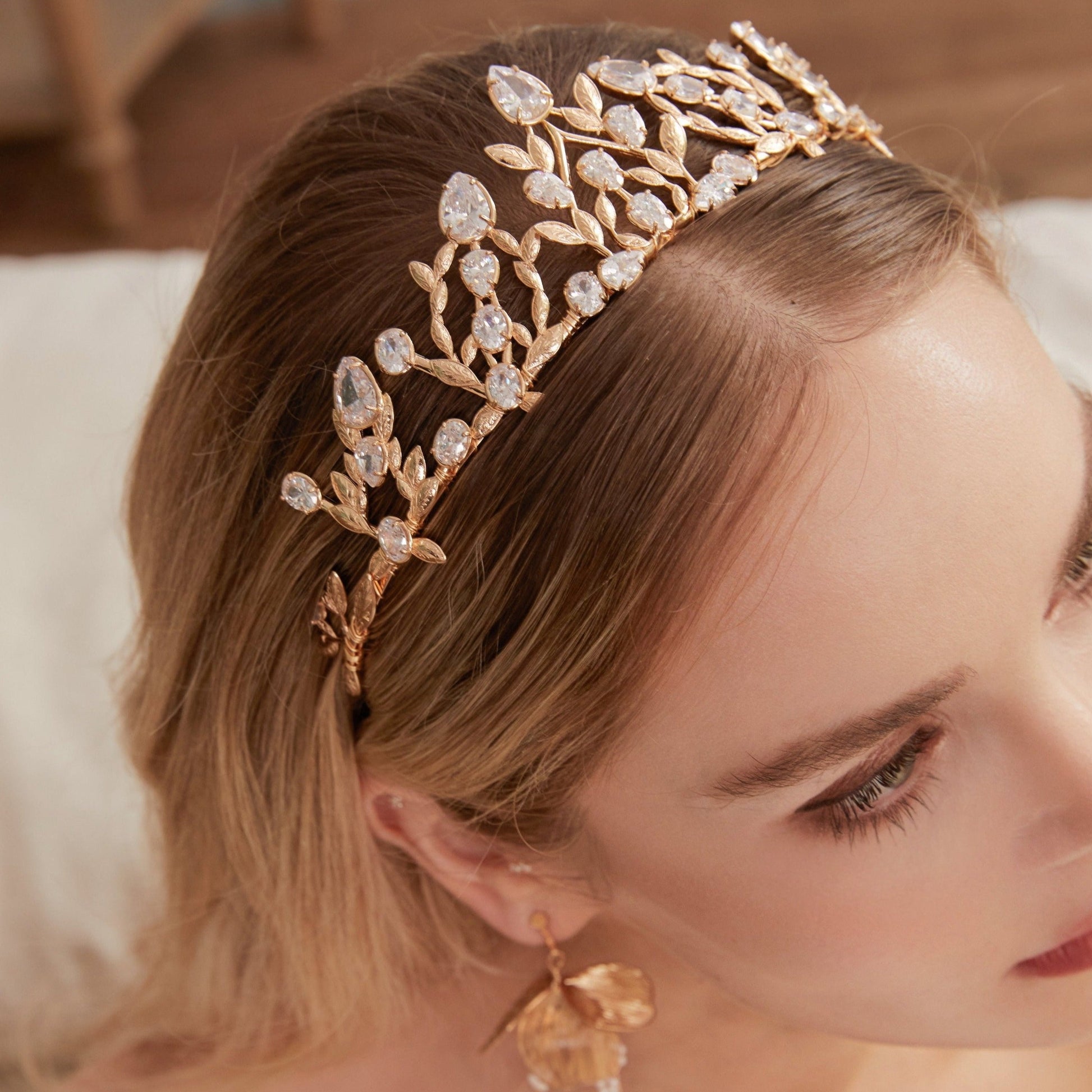 Victoria | Gold Crystal Bridal Crown Tiara - Handcrafted with attention to detail, this unique crown features delicate gold metal leaves intricately arranged alongside an array of dazzling rhinestone flowers in various sizes. The combination of gold and crystals creates a vintage-inspired woodland feel.