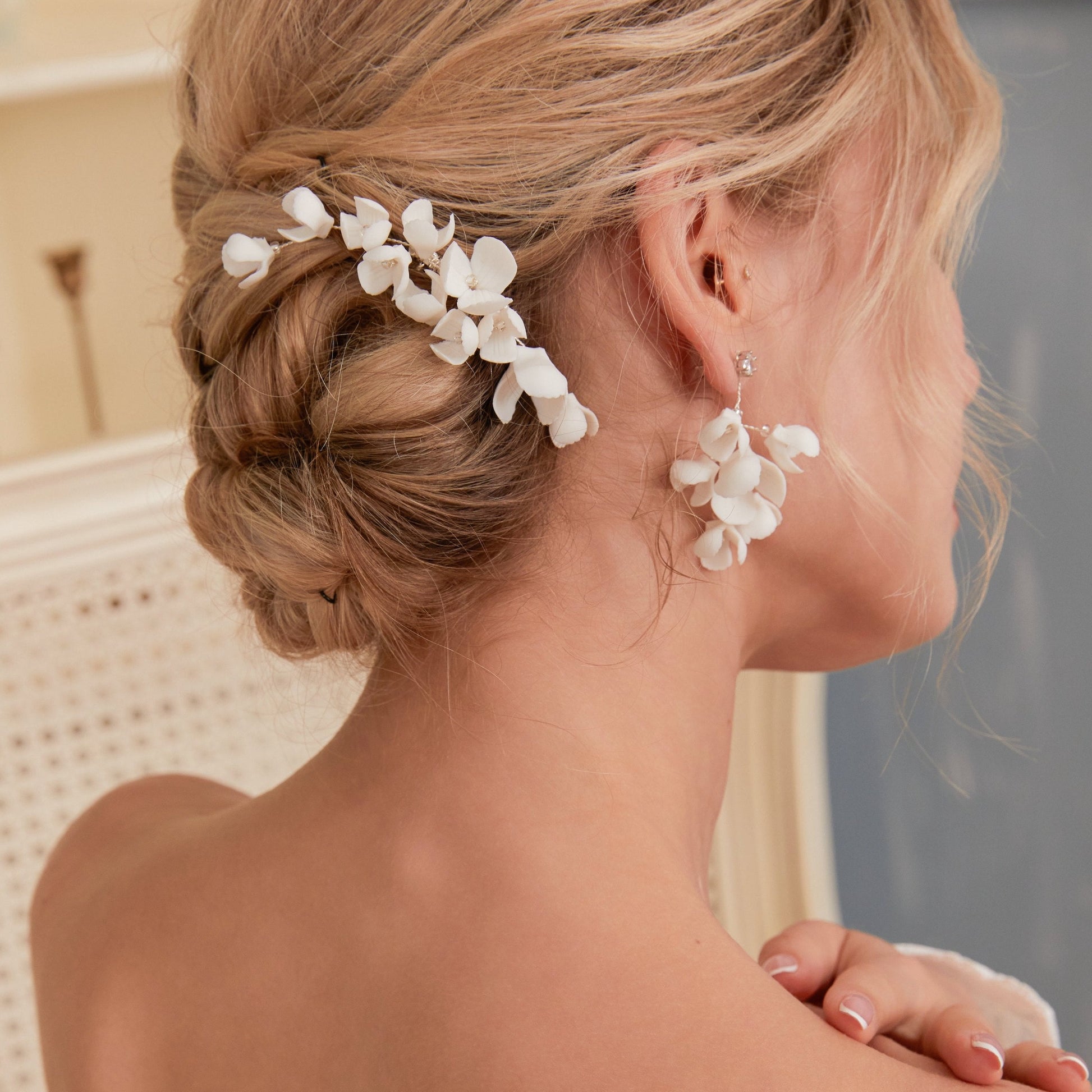 These handcrafted flower bridal earrings are designed to make a statement with their elegant long drop design. Each earring features a cluster of ivory clay blossoms and flowers that gracefully drape from a shimmering rhinestone.