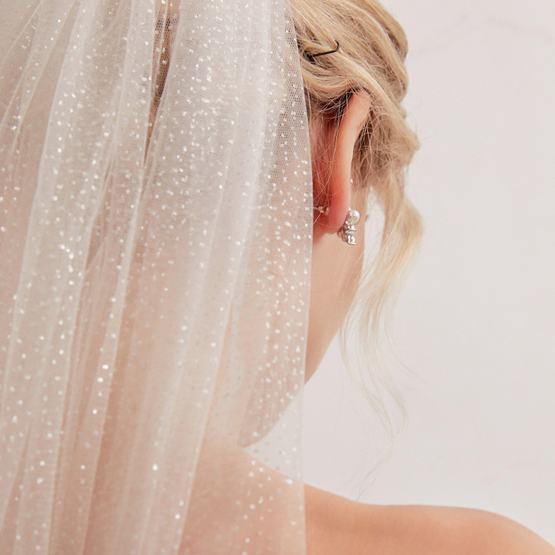 Luxurious single-layer cathedral wedding veil crafted from delicate sparkle glitter tulle. With an ivory base (also available in white and champagne), it features a simple cut edge for an elegant and timeless style that complements any bridal look.  At 3 meters long, this veil is the perfect bridal accessory to enhance any wedding dress. Offering a subtle sparkle without any fuss, it adds a touch of glamour to your special day.