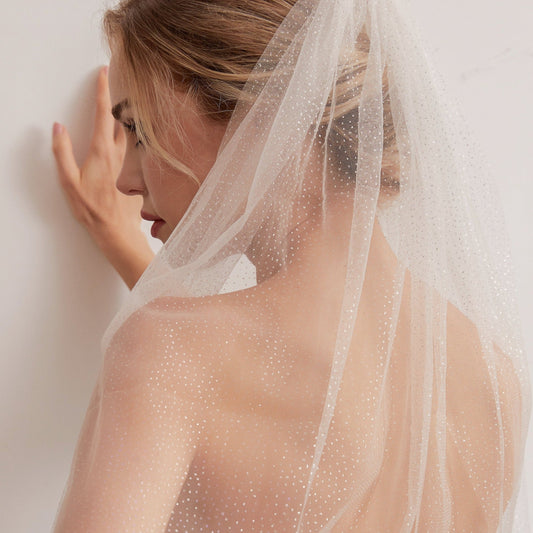 Luxurious single-layer cathedral wedding veil crafted from delicate sparkle glitter tulle. With an ivory base (also available in white and champagne), it features a simple cut edge for an elegant and timeless style that complements any bridal look.  At 3 meters long, this veil is the perfect bridal accessory to enhance any wedding dress. Offering a subtle sparkle without any fuss, it adds a touch of glamour to your special day.