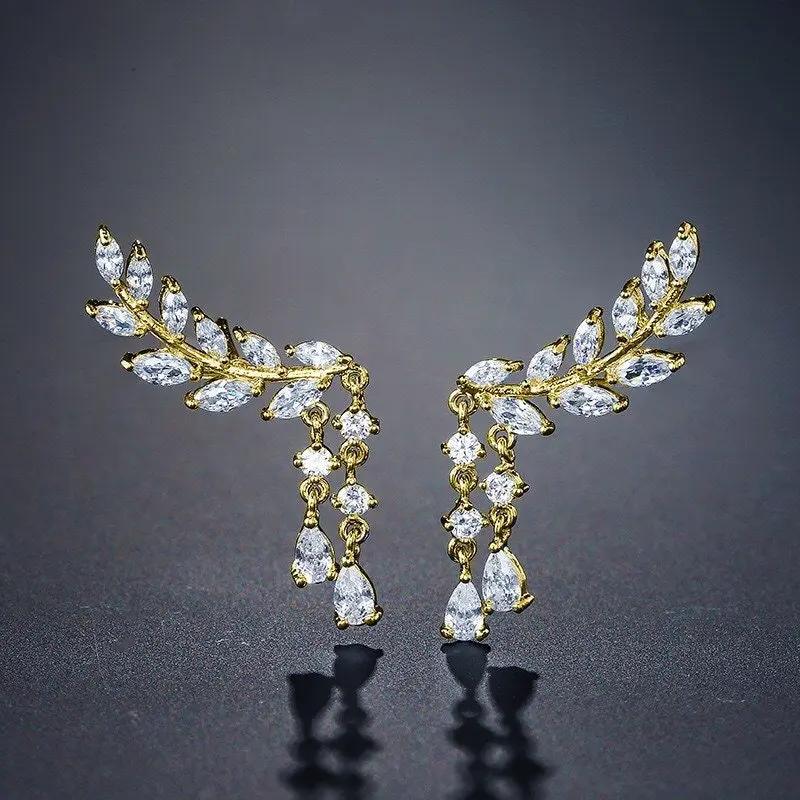 Pair of gold olive leaf climber earrings on a dark grey background