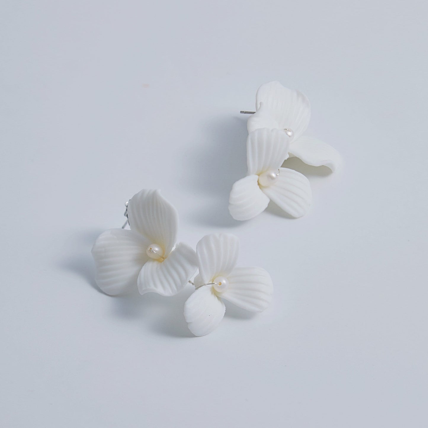 Skillfully handcrafted, these flower bridal earrings are the perfect complement to our signature porcelain headpieces. Each earring is exquisitely made by hand, featuring two delicate white clay flowers adorned with freshwater pearls.