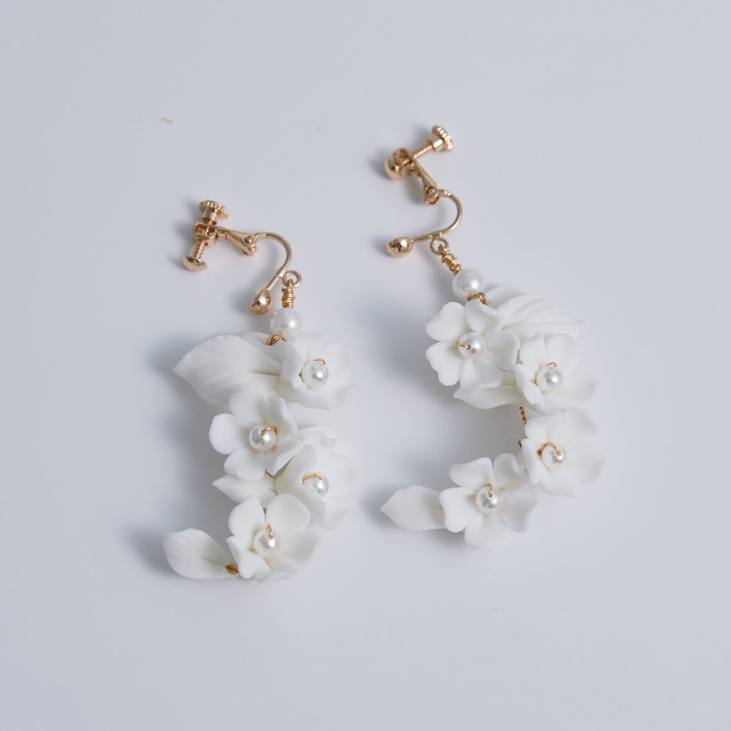 Carefully crafted by hand, these flower bridal earrings are a perfect match to our porcelain headpieces. Each earring features delicate white clay flowers and leaves adorned with shimmering freshwater pearls. These earrings have a long drop design that is sure to catch attention and make a statement.