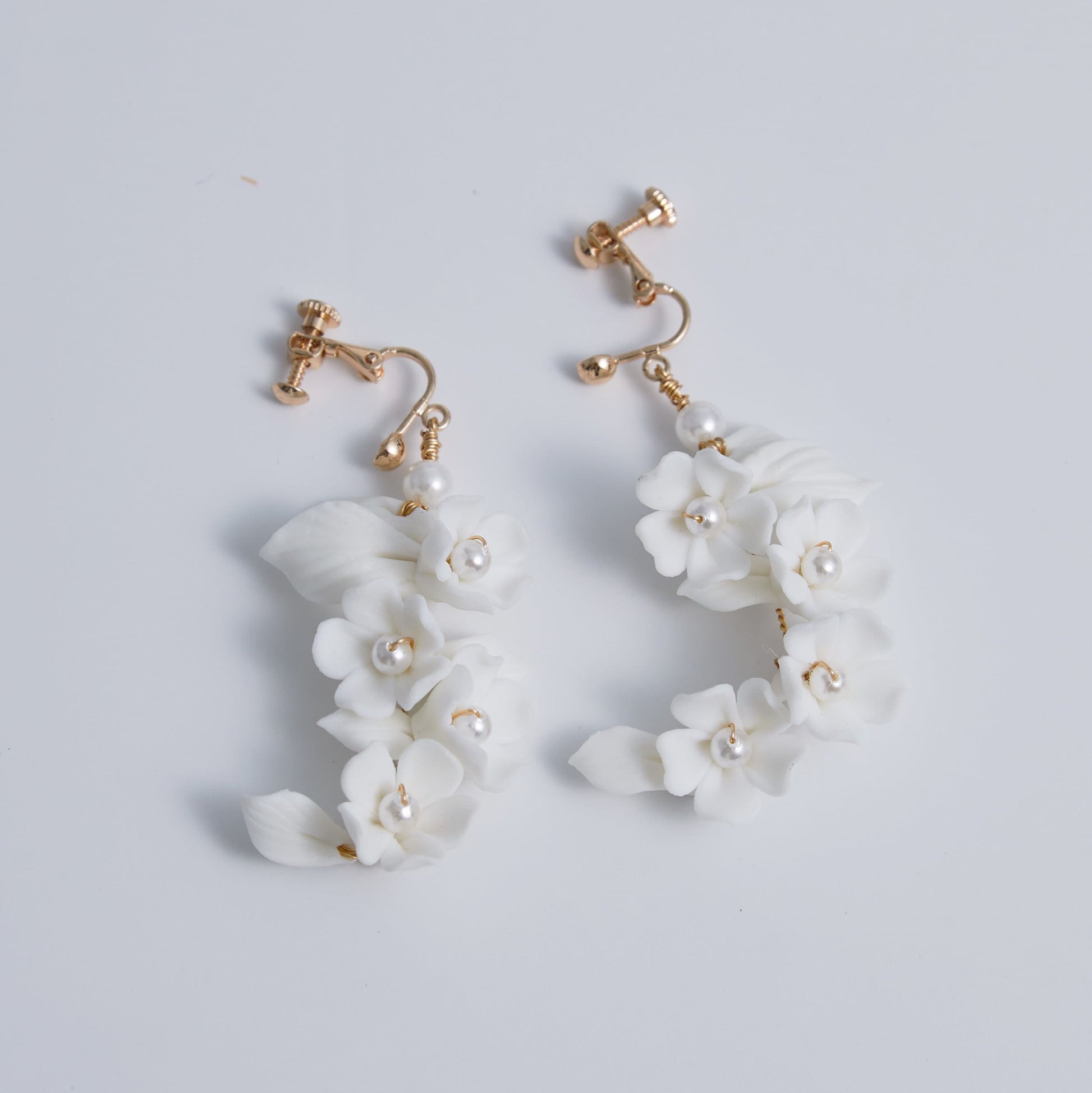 Carefully crafted by hand, these flower bridal earrings are a perfect match to our porcelain headpieces. Each earring features delicate white clay flowers and leaves adorned with shimmering freshwater pearls. These earrings have a long drop design that is sure to catch attention and make a statement.