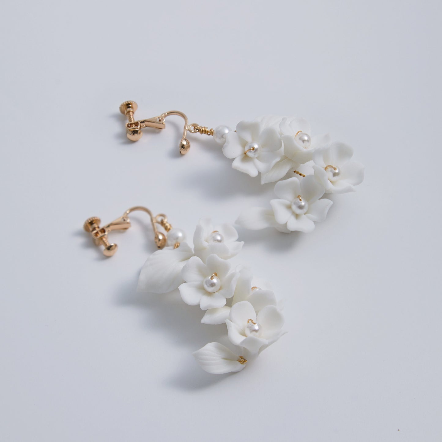 Carefully crafted by hand, these flower bridal earrings are a perfect match to our porcelain headpieces. Each earring features delicate white clay flowers and leaves adorned with shimmering freshwater pearls. These earrings have a long drop design that is sure to catch attention and make a statement.