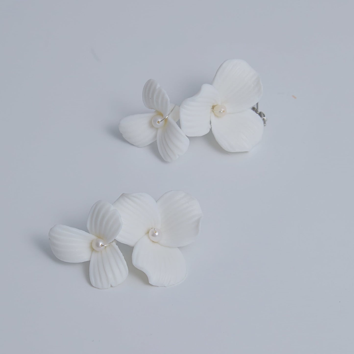 Skillfully handcrafted, these flower bridal earrings are the perfect complement to our signature porcelain headpieces. Each earring is exquisitely made by hand, featuring two delicate white clay flowers adorned with freshwater pearls.