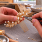 AI-generated making illustration showing hands working on a single gold leaf and white bead bridal hair comb