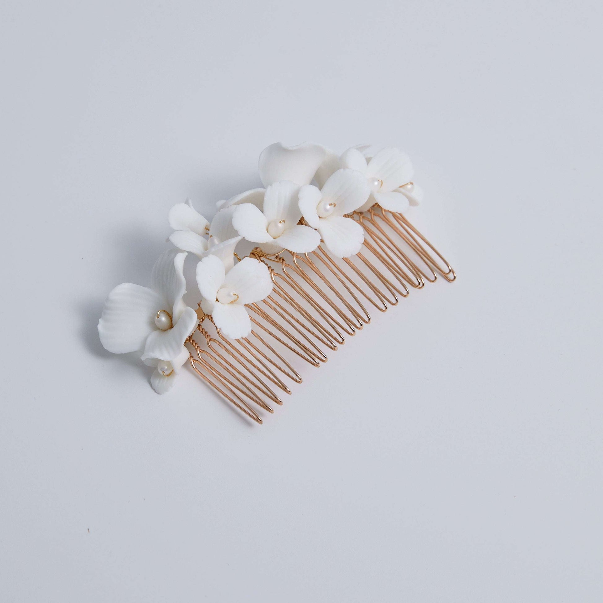 A delicate and romantic white porcelain bridal hair comb, handcrafted with love. This exquisite bridal hairpiece features a cluster of beautiful flowers adorned with lustrous natural freshwater pearls, arranged in a full design.