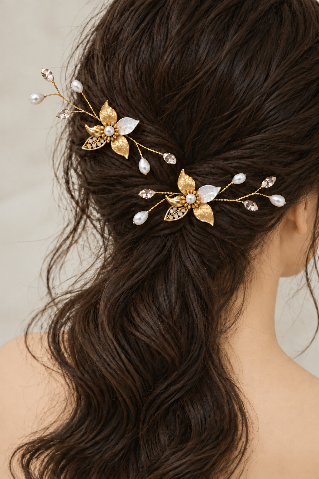 Side-rear view of two gold pearl and CZ leaf hair combs above loose bridal waves