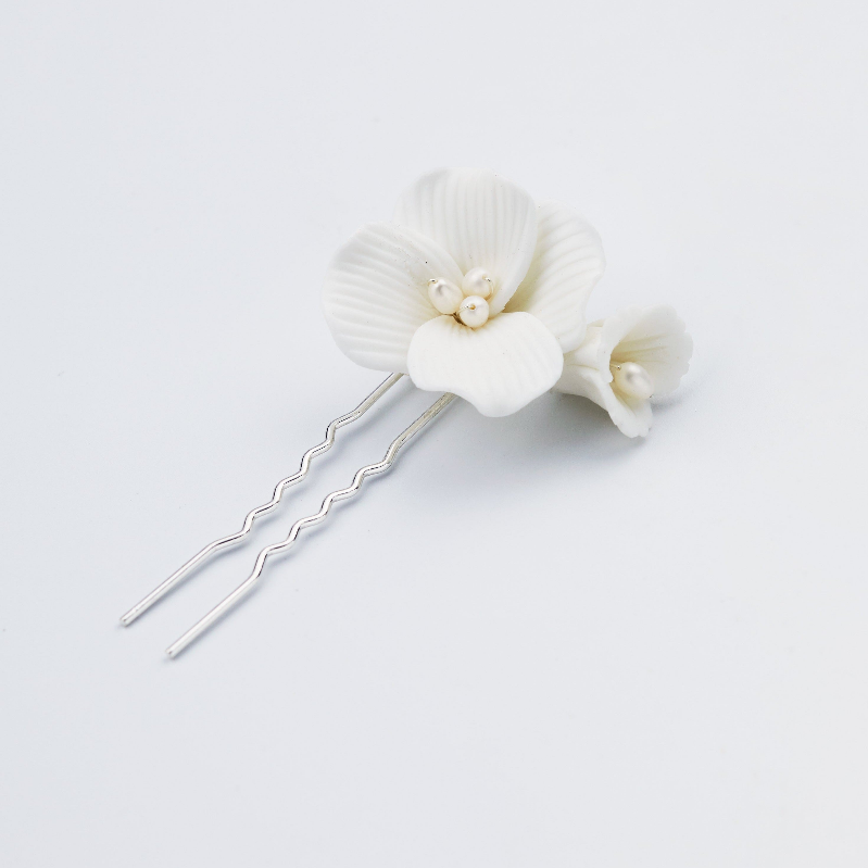 Two silver hair pins decorated with white ceramic or resin orchid flowers and small pearl-like beads, photographed on a clean white background.
