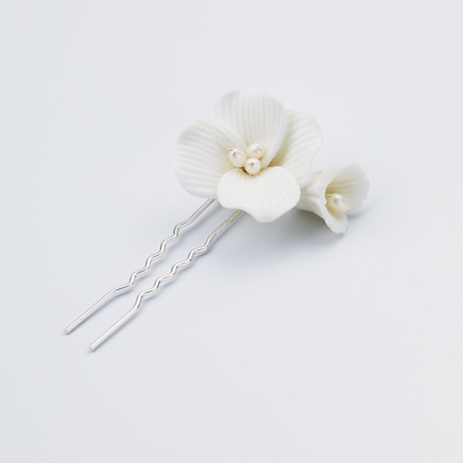 Two silver hair pins decorated with white ceramic or resin orchid flowers and small pearl-like beads, photographed on a clean white background.