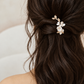 White ceramic flower and gold leaf bridal hair clip worn in a brown half-up hairstyle, close rear view