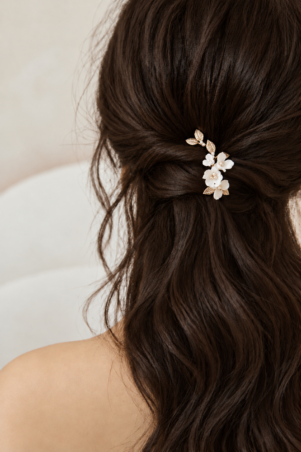 White ceramic flower and gold leaf bridal hair clip worn in a brown half-up hairstyle, close rear view