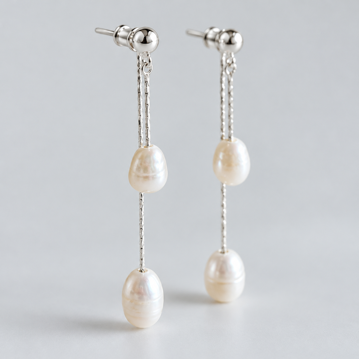 Pair of freshwater pearl tassel earrings with two pearls on each, photographed against pale grey