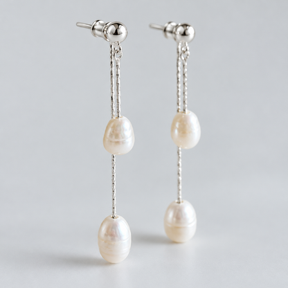 Pair of freshwater pearl tassel earrings with two pearls on each, photographed against pale grey