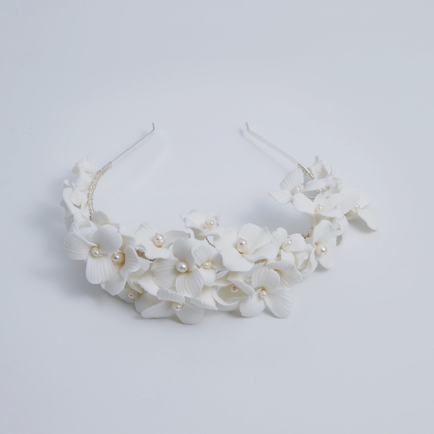 A gloriously romantic hand-sculpted porcelain bridal crown. Made with an arrangement of individually crafted flowers and dainty pearls. This full and textured headband makes a statement but yet still feels incredibly feminine.