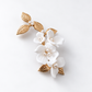 Single white ceramic flower bridal hair clip with gold leaves on a pale grey background