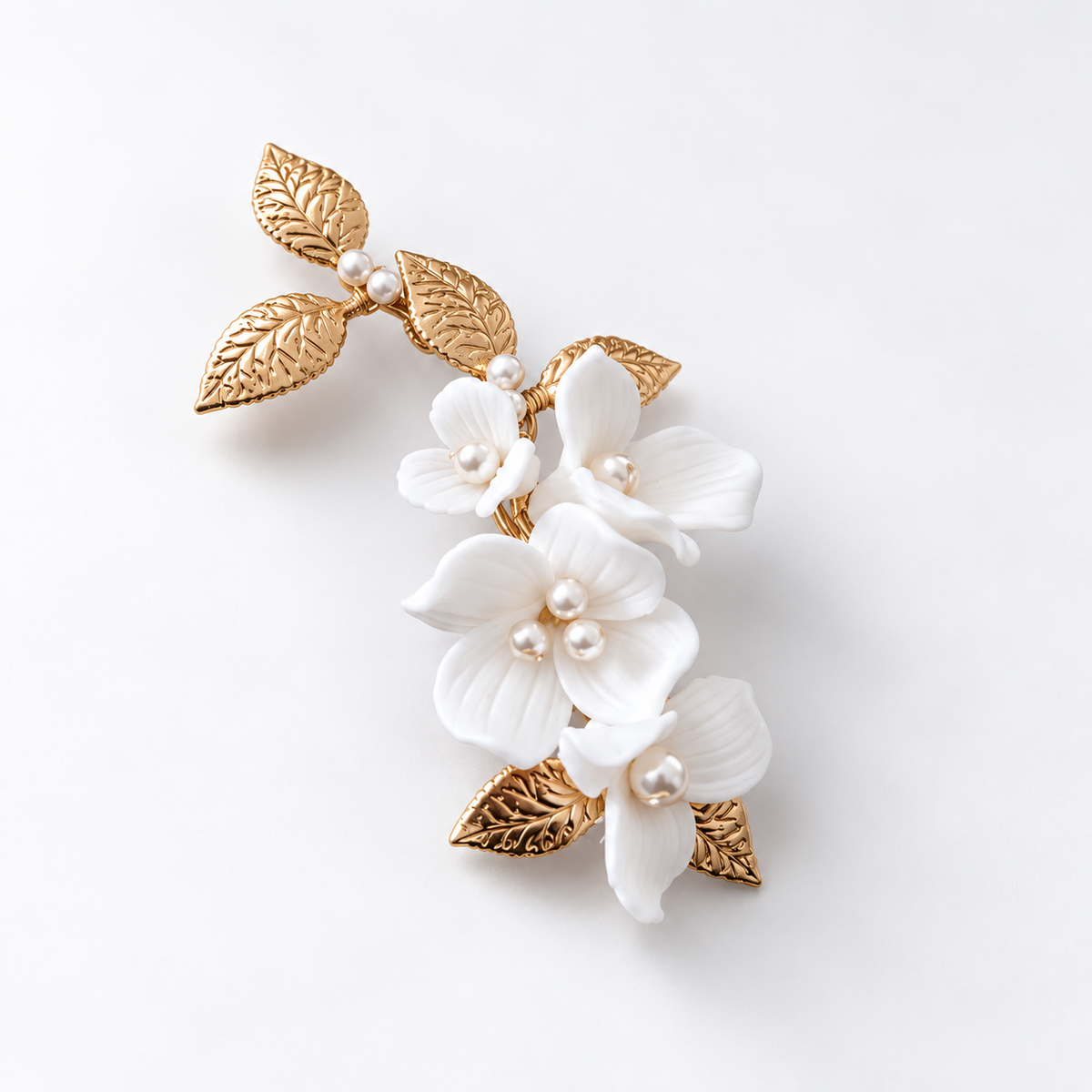 Single white ceramic flower bridal hair clip with gold leaves on a pale grey background