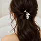 White ceramic flower hair clip worn above long brown bridal curls, wider rear view