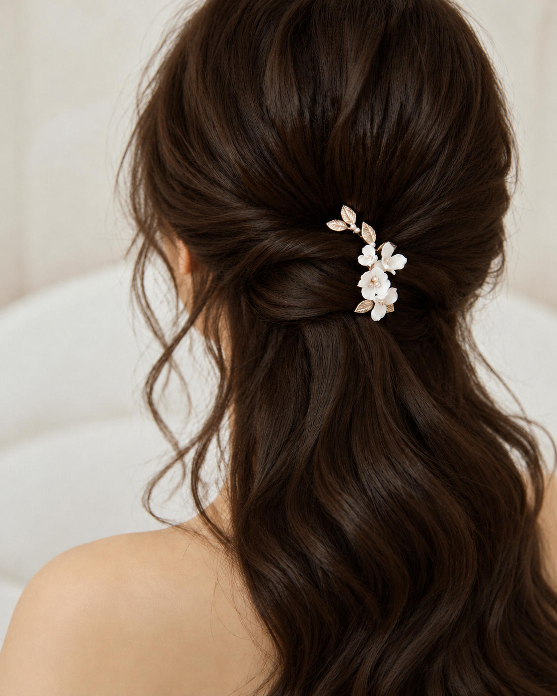 White ceramic flower hair clip worn above long brown bridal curls, wider rear view