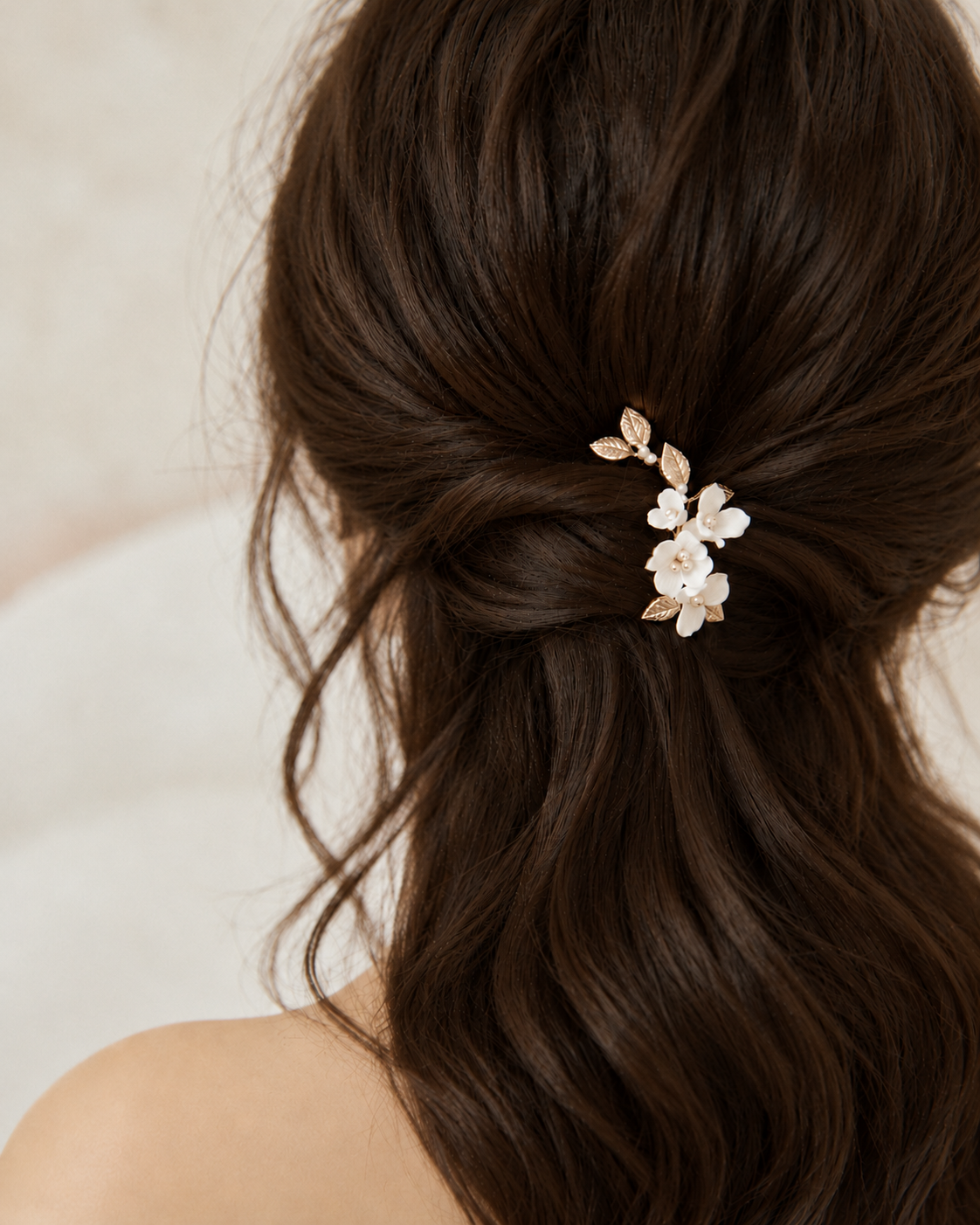 Rear view of a ceramic flower and gold leaf hair clip in a twisted half-up bridal hairstyle