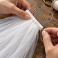 Close-up of a metal hair comb with a white fabric-covered base being attached to gathered veil tulle