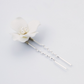 A white flower hair pin with two silver spiral pins and small pearl-like accents in the center, photographed on a clean light gray background.