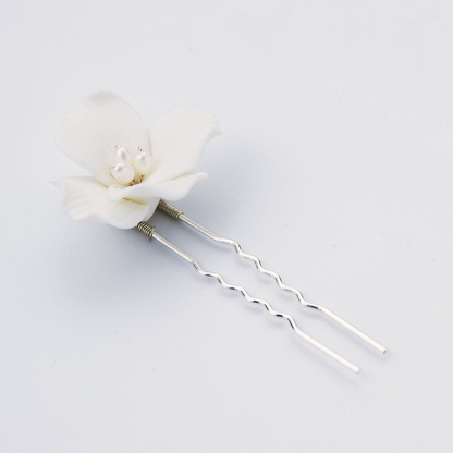 A white flower hair pin with two silver spiral pins and small pearl-like accents in the center, photographed on a clean light gray background.