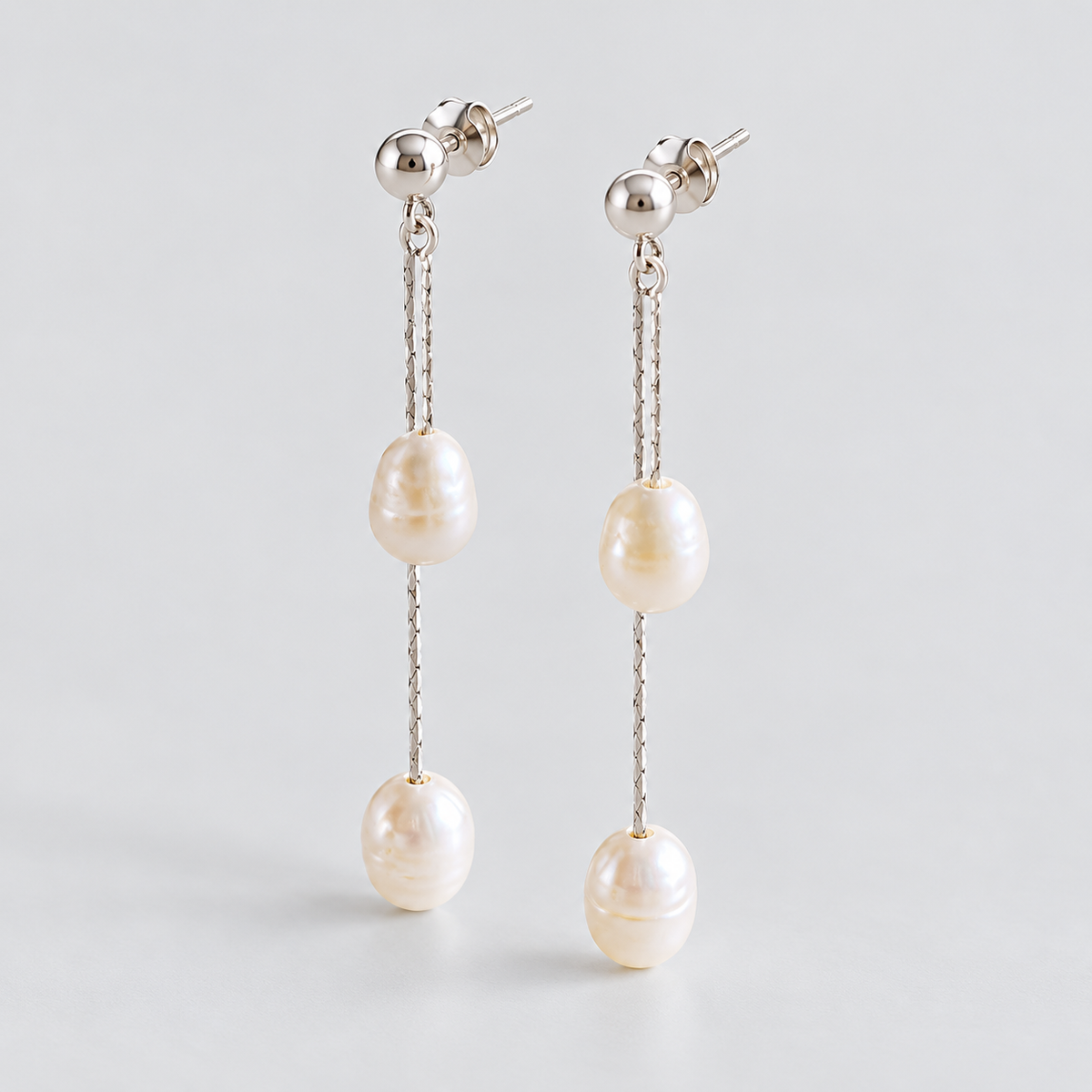 Angled view of the pair showing stud posts, fine chains and two pearls per earring