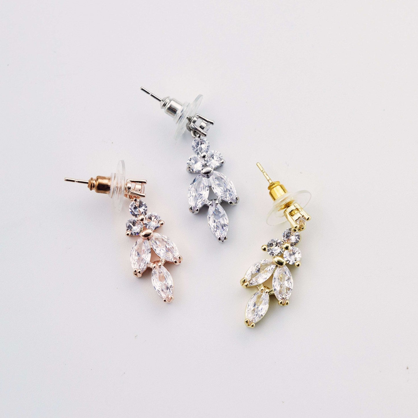 Three pairs of leaf drop earrings in silver, gold, and rose gold on a white background