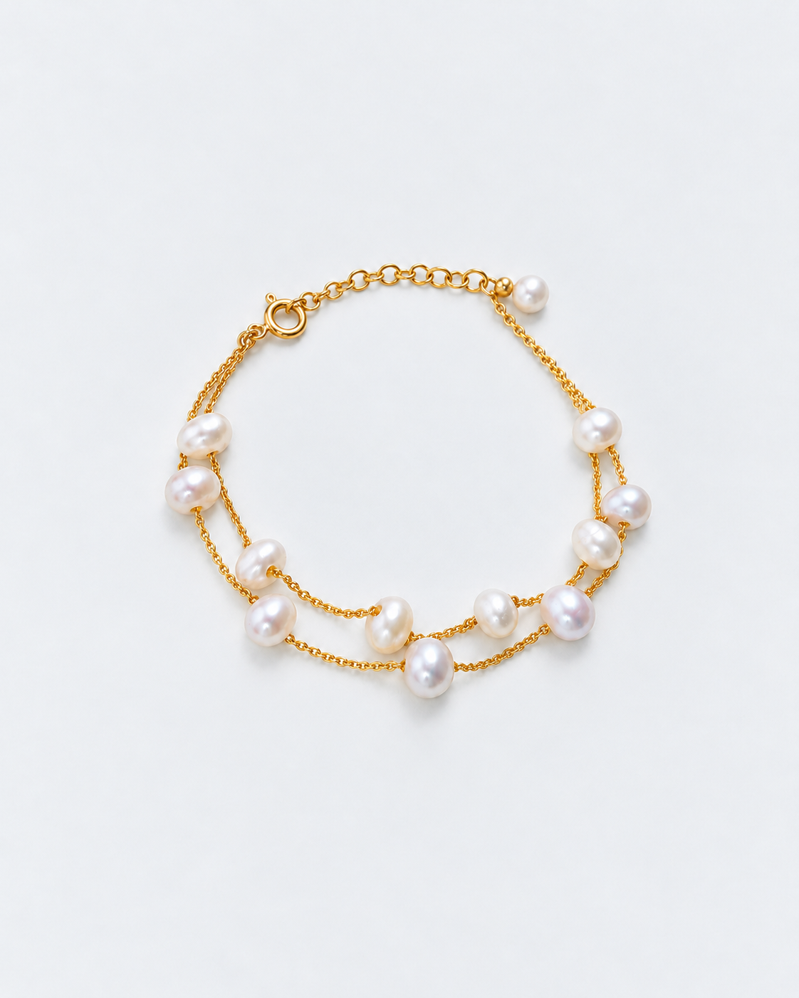 Double-strand freshwater pearl bracelet with gold chains, full view on a pale grey background