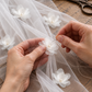 Close-up of layered white fabric flowers with pearl-like centres being stitched onto sheer tulle