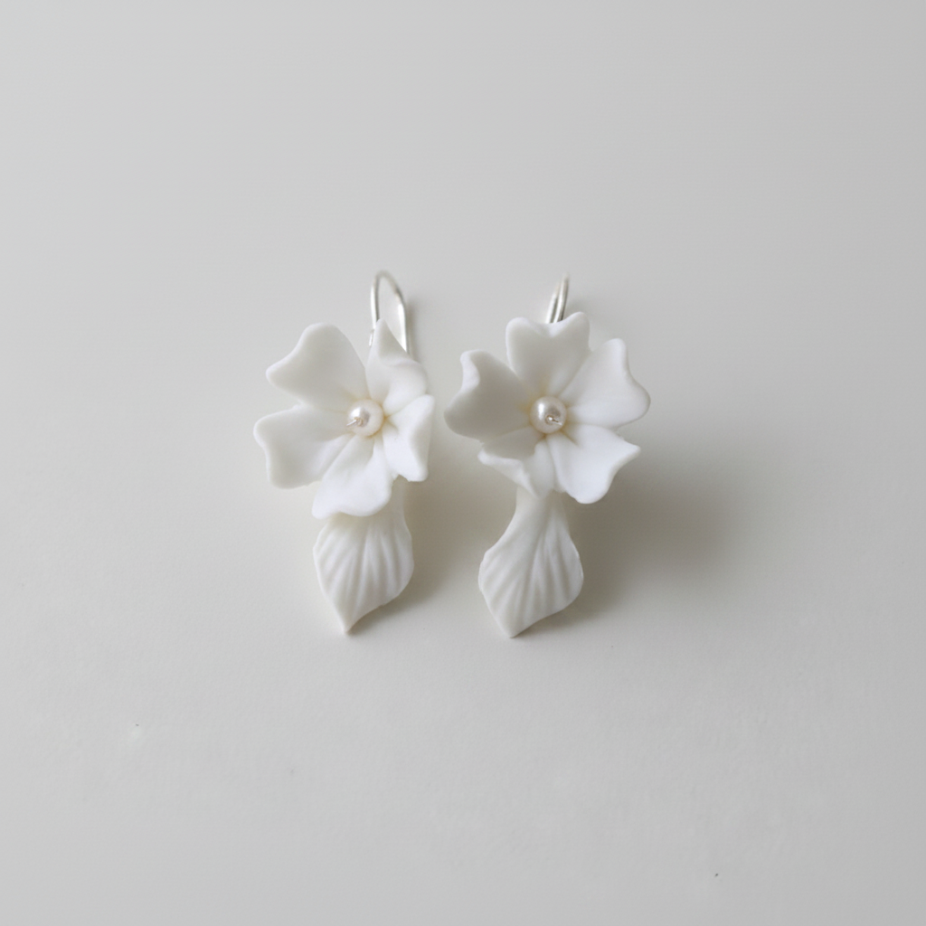 White porcelain flower drop earrings with pearl centre and ceramic leaf drop — bridal jewellery flat lay
