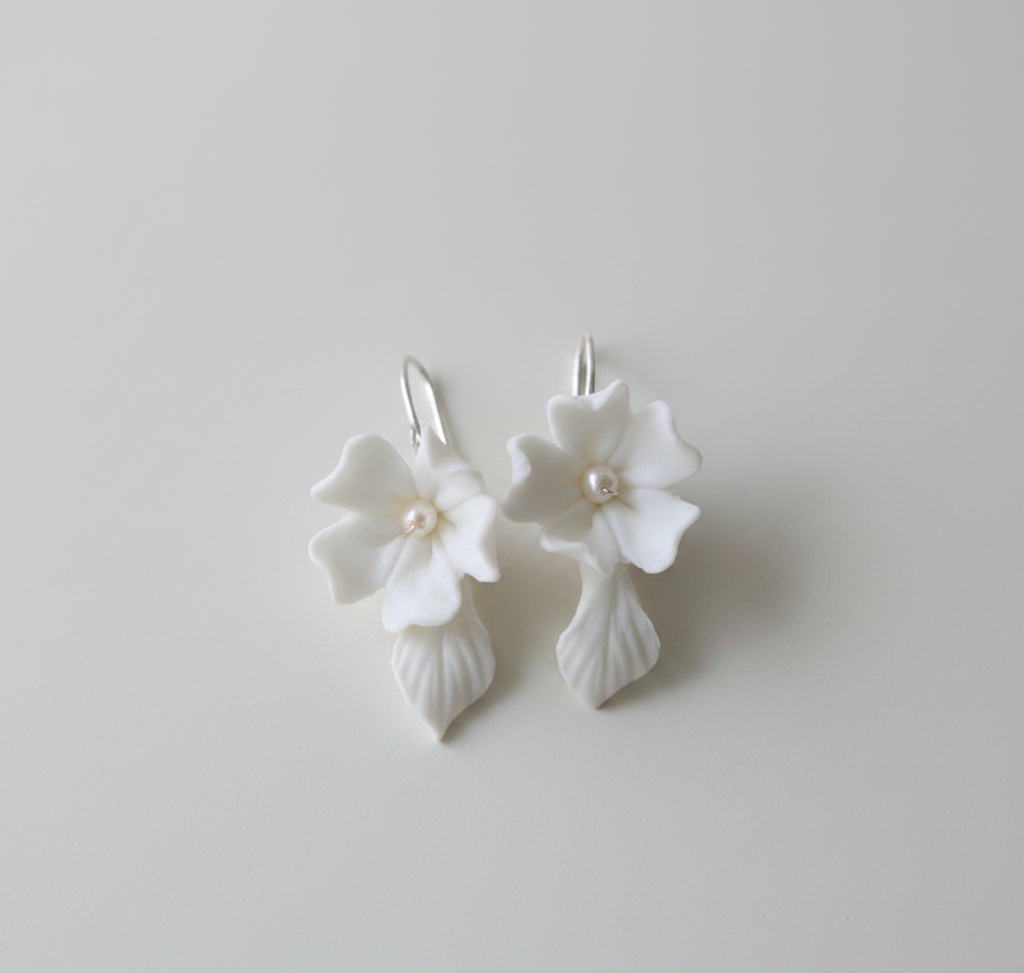 Pair of white porcelain hydrangea drop earrings with pearl and leaf drop on light grey background — wedding earrings UK