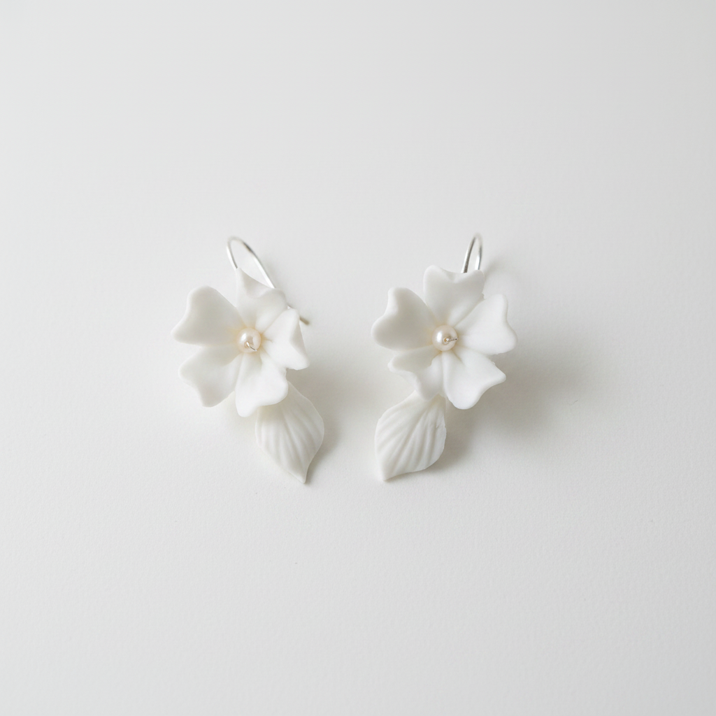 White porcelain flower drop earrings with pearl centre and ceramic leaf drop — bridal jewellery flat lay