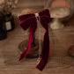 Burgundy velvet bow hair clip with black veil and rhinestone drops on a wooden background