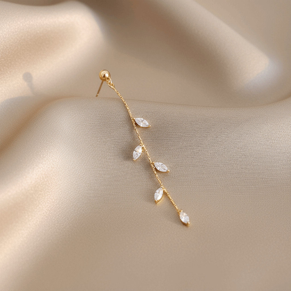 14K gold olive leaf crystal drop earring macro close-up on champagne silk background