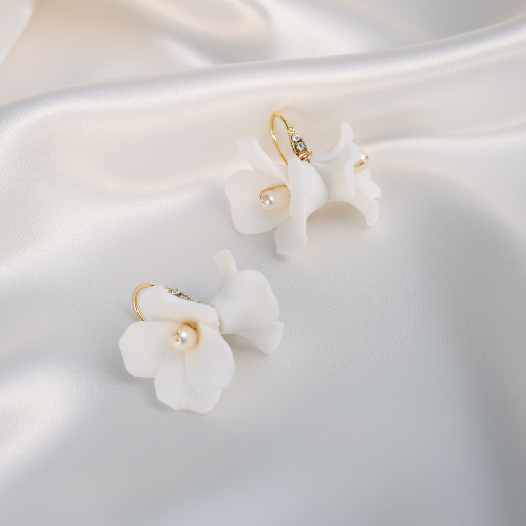 White porcelain flower earrings with gold hooks and pearl centers on draped white silk fabric, luxury bridal jewelry
