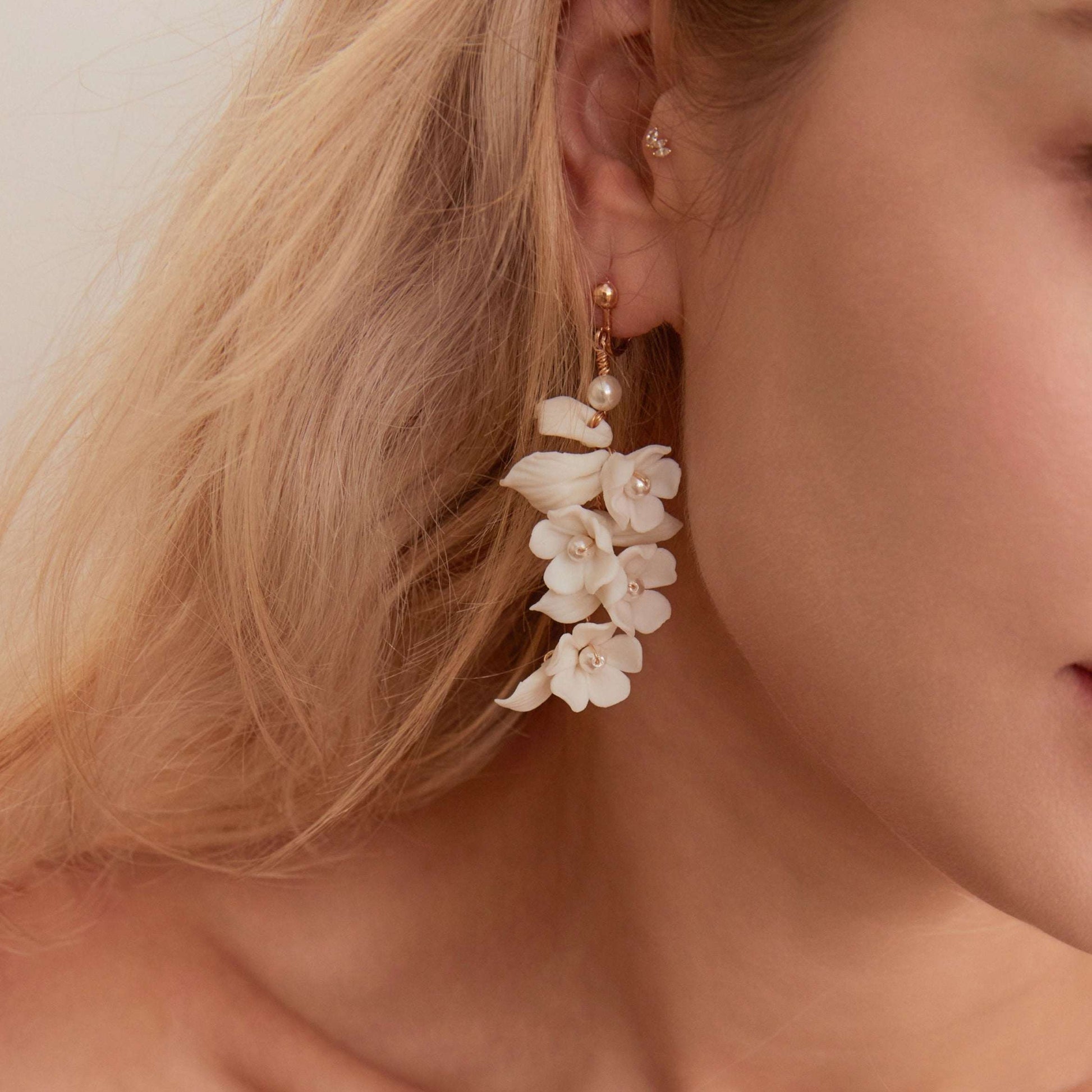 Carefully crafted by hand, these flower bridal earrings are a perfect match to our porcelain headpieces. Each earring features delicate white clay flowers and leaves adorned with shimmering freshwater pearls. These earrings have a long drop design that is sure to catch attention and make a statement.
