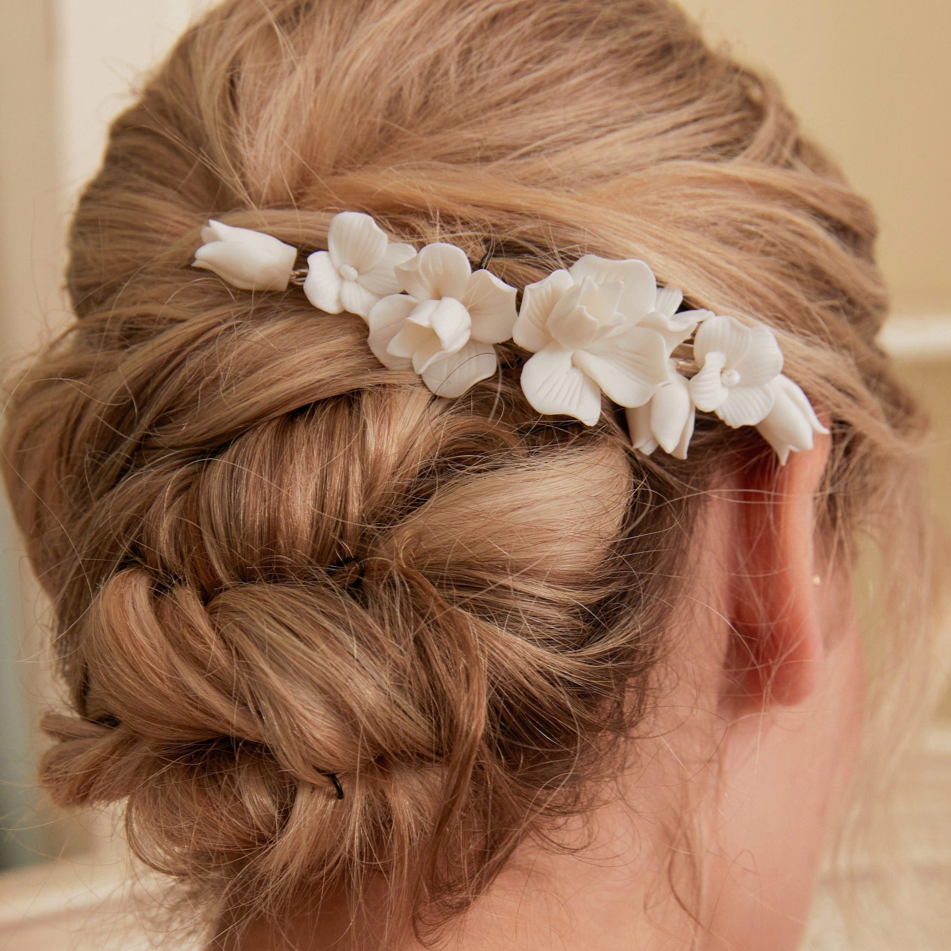 This statement bridal hair clip features carefully handcrafted white porcelain flowers and blossoms, adding an elegant and romantic touch to your hairstyle. It effortlessly enhances any bridal look, creating a timeless style.