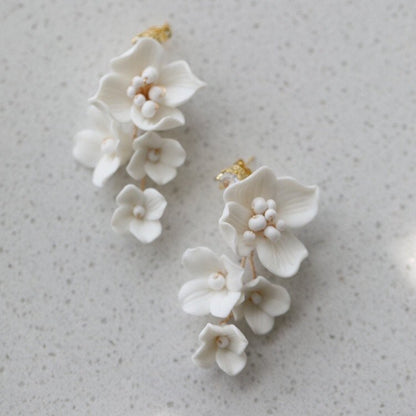 Handmade white porcelain flower earrings with crystal studs on a white surface
