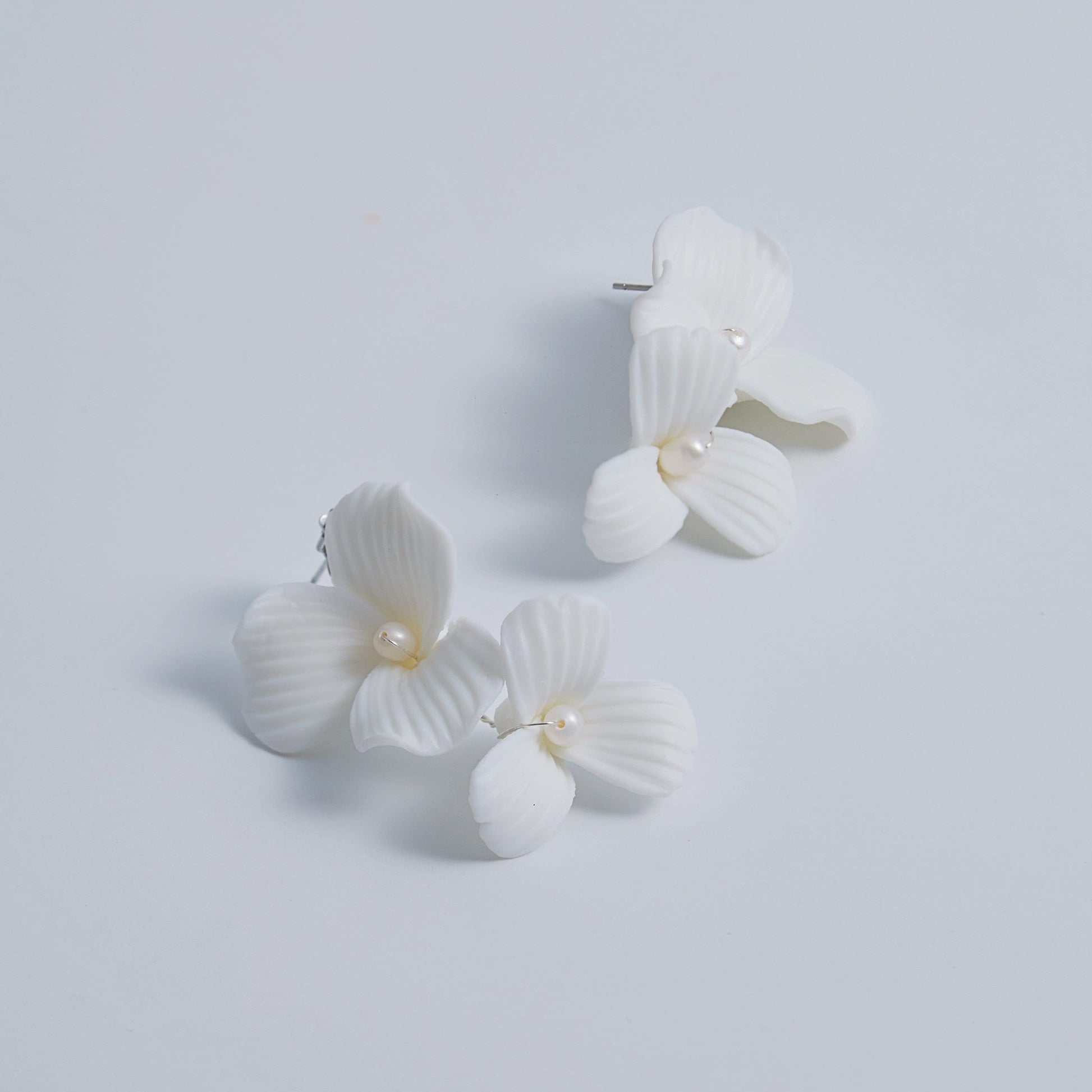 Skillfully handcrafted, these flower bridal earrings are the perfect complement to our signature porcelain headpieces. Each earring is exquisitely made by hand, featuring two delicate white clay flowers adorned with freshwater pearls.